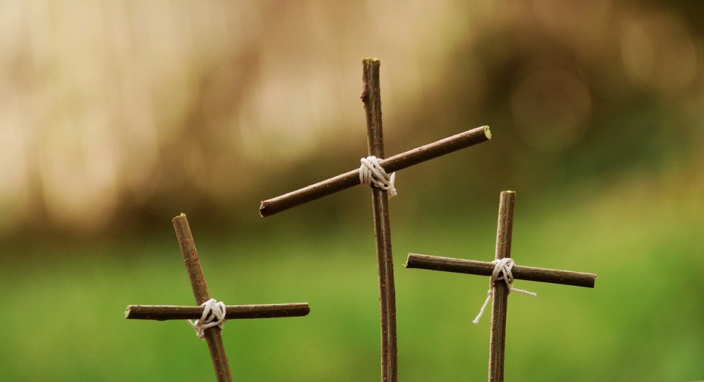 Three small wooden crosses tied together with twine against a blurred green background.