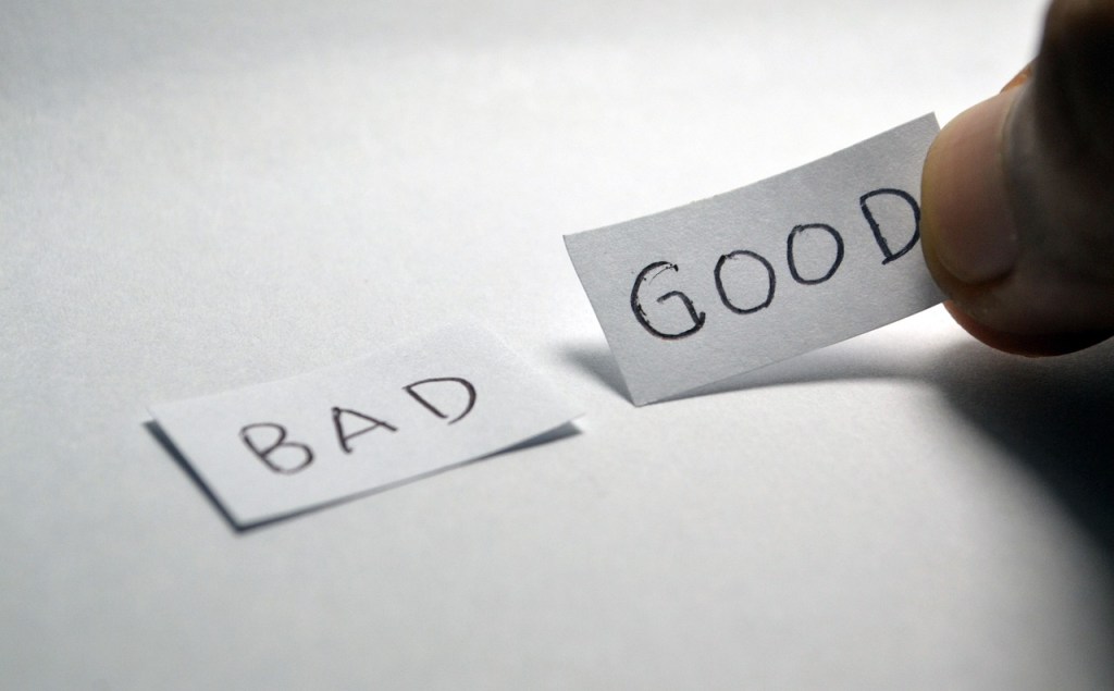 A hand holding a paper labeled 'GOOD' while another paper labeled 'BAD' lies on a surface.