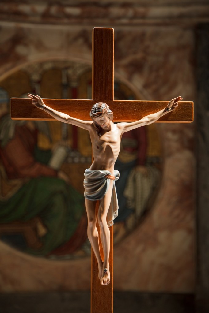 A crucifix depicting Jesus Christ on the cross, with a wooden cross and an artistic background.