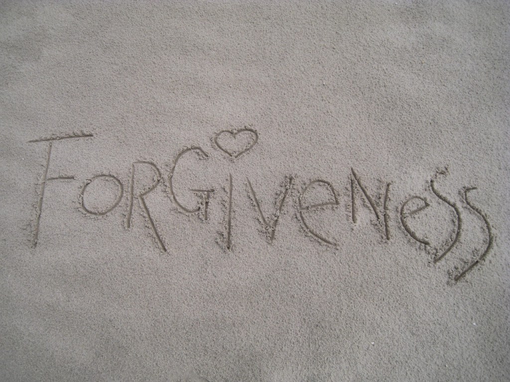 The word 'Forgiveness' written in the sand with a heart symbol included in the letters.