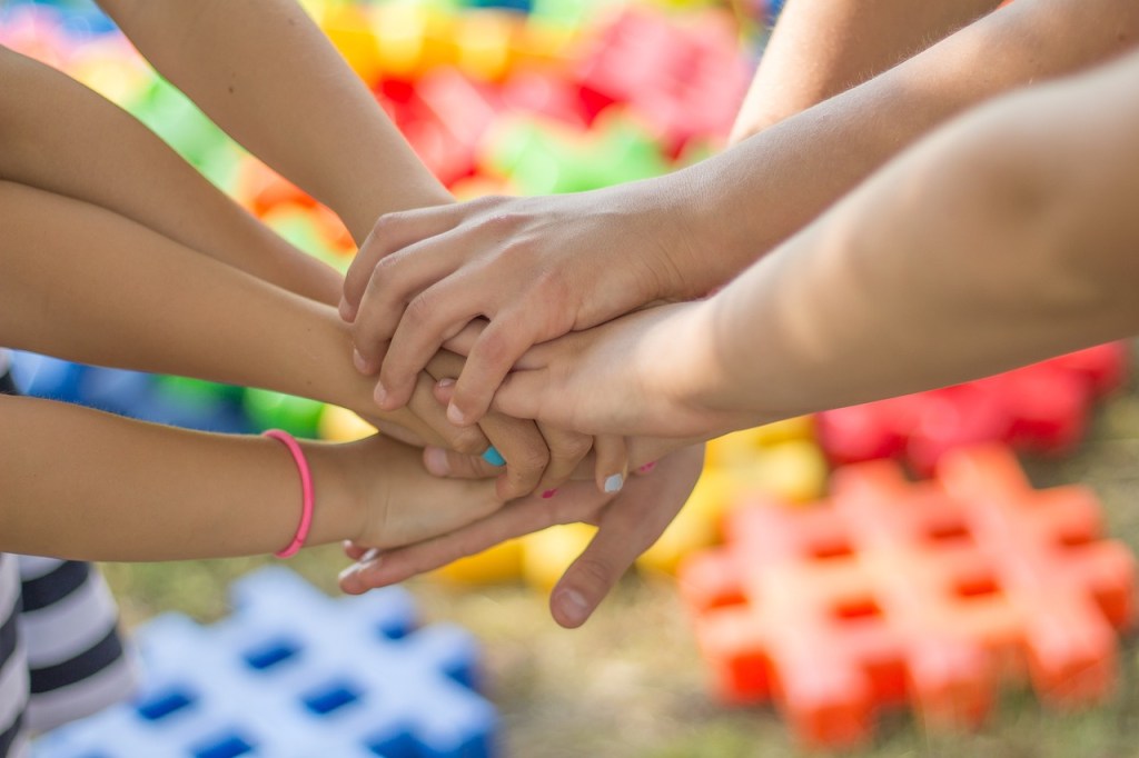 A close-up of multiple hands stacking together, symbolizing friendship and unity, with colorful background elements.