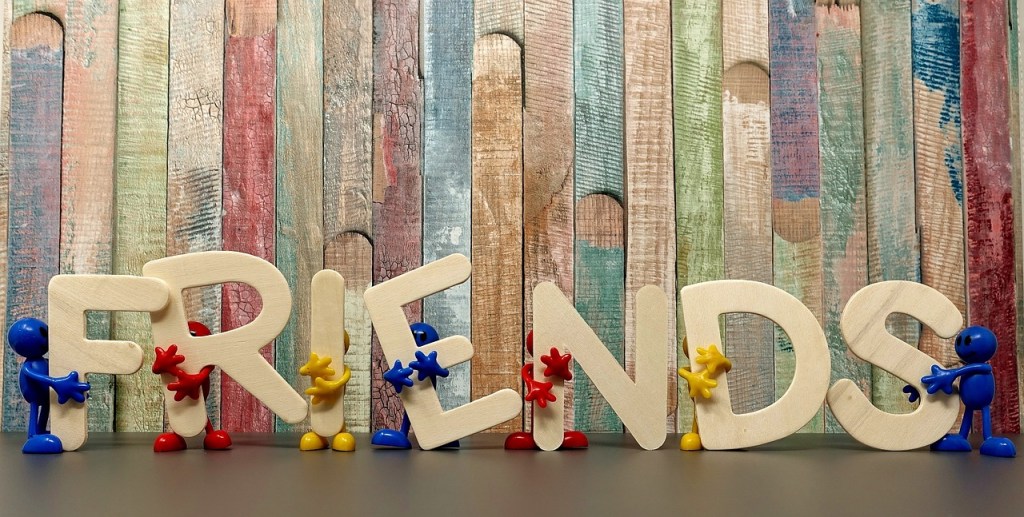 Colorful wooden letters spelling 'FRIENDS' with small figurines holding the letters, set against a textured, multicolored wooden background.