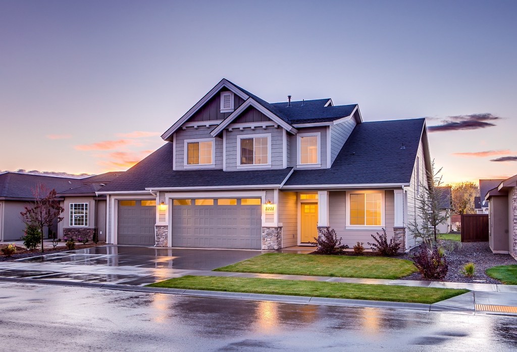 A modern two-story house with a well-manicured lawn and driveway, captured during sunset with vibrant colors in the sky.