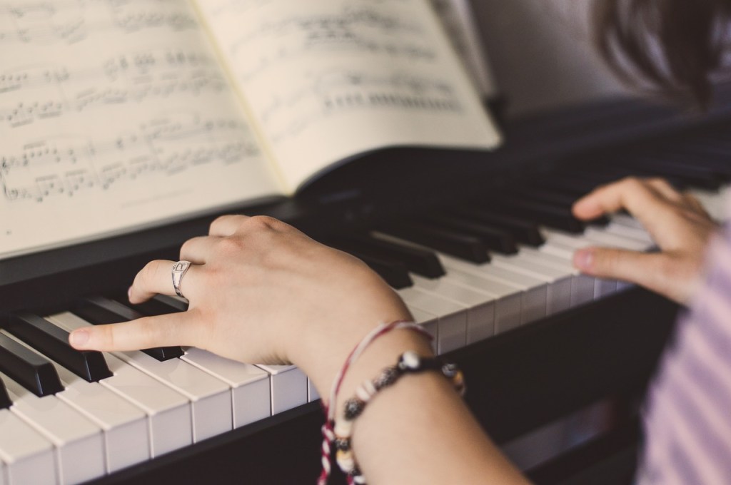 A close-up of hands playing a piano with sheet music visible in the background.