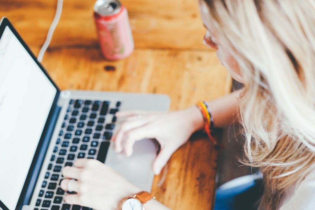 A person typing on a laptop with a can of soda on a wooden table.