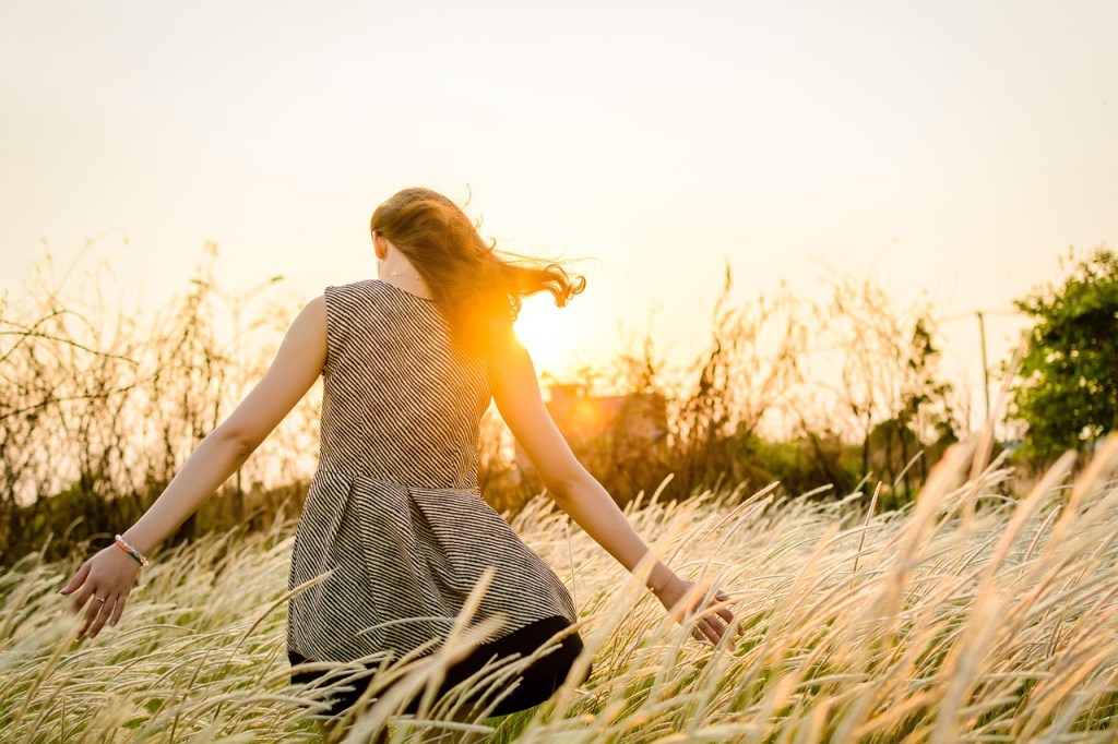 A young woman running through a field of tall grass during sunset, her hair flowing and a warm glow illuminating the scene.