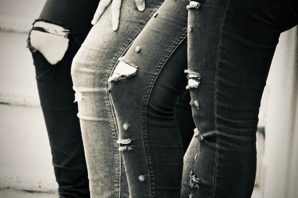 Close-up of the legs of three individuals wearing distressed jeans, showcasing various rips and embellishments.