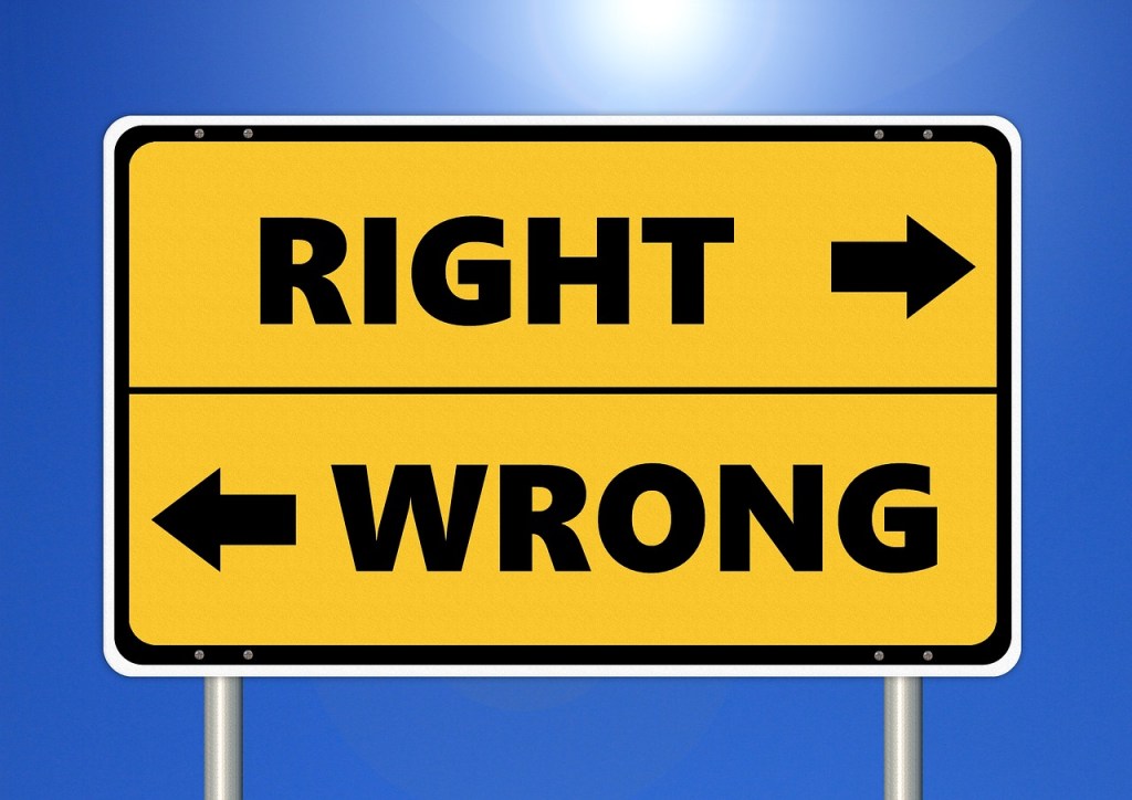 A yellow road sign with the words 'RIGHT' pointing to the right and 'WRONG' pointing to the left, set against a blue sky.