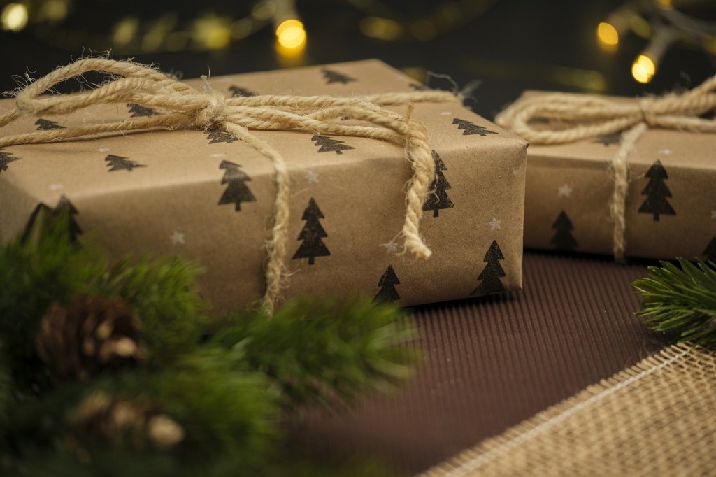 Two beautifully wrapped gifts in brown paper with evergreen tree patterns, tied with twine, accompanied by pine branches.