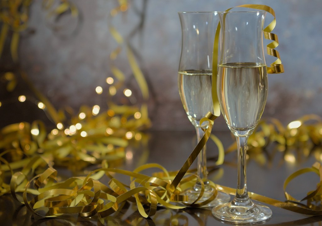 Two champagne glasses decorated with golden ribbons, surrounded by festive golden streamers.