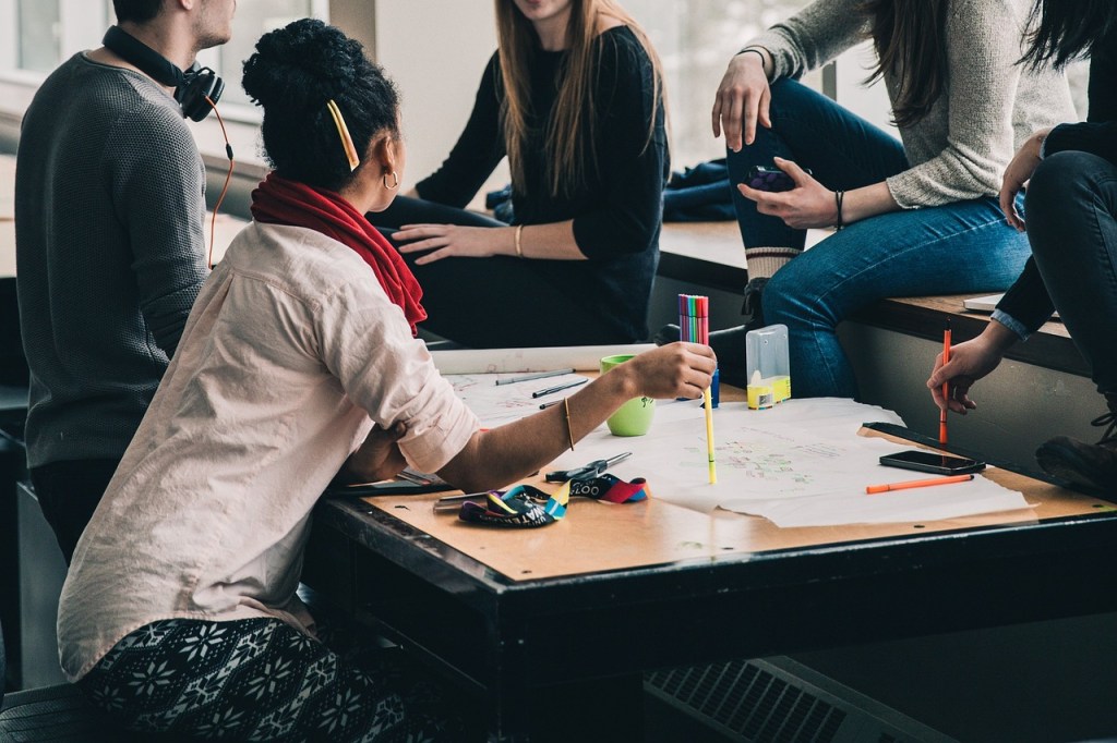 A diverse group of students engaged in a collaborative project at a table, with colorful markers and paper spread out, showcasing a creative workspace.