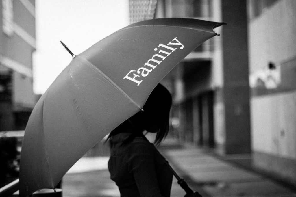 A person holding a red umbrella with the word 'Family' printed on it, standing in an urban setting.
