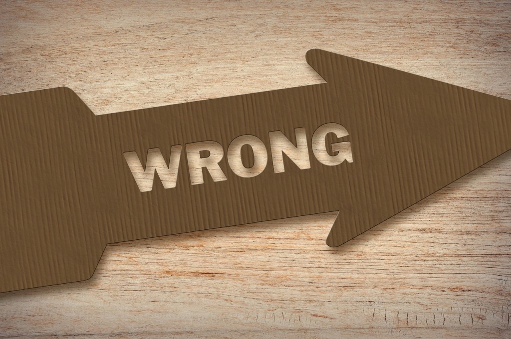A cardboard arrow pointing right with the word 'WRONG' carved into it, placed on a wooden background.