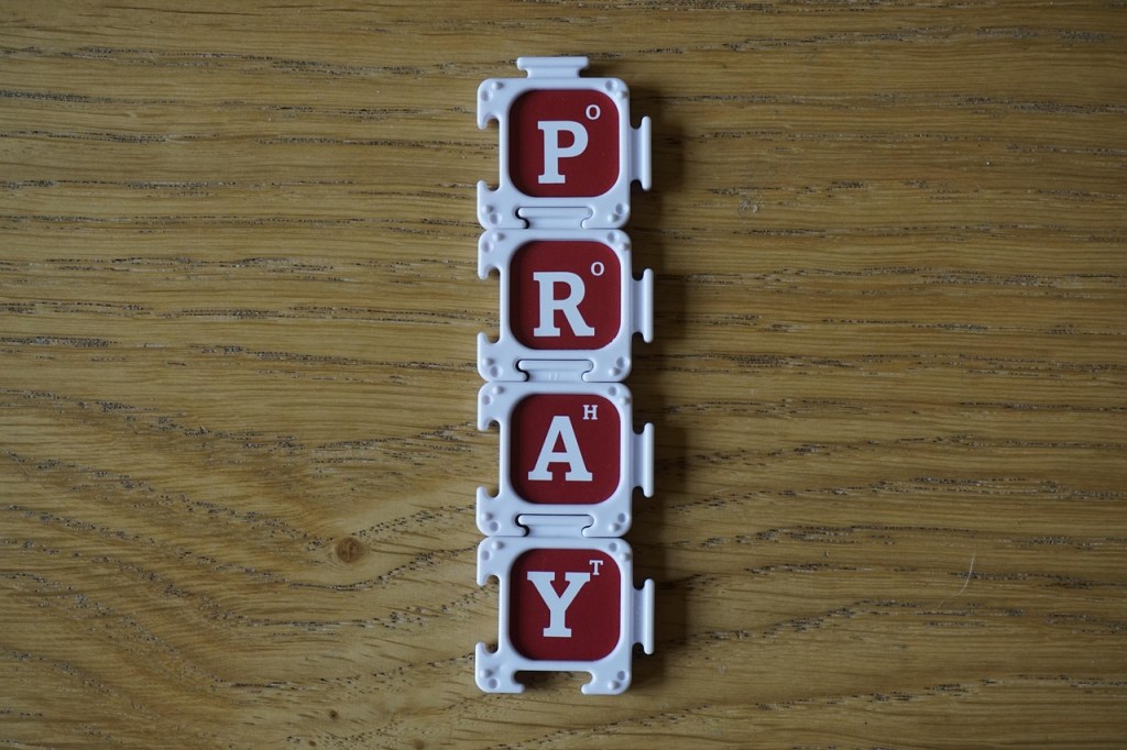 Colorful tiles arranged vertically spelling the word 'PRAY' on a wooden surface.