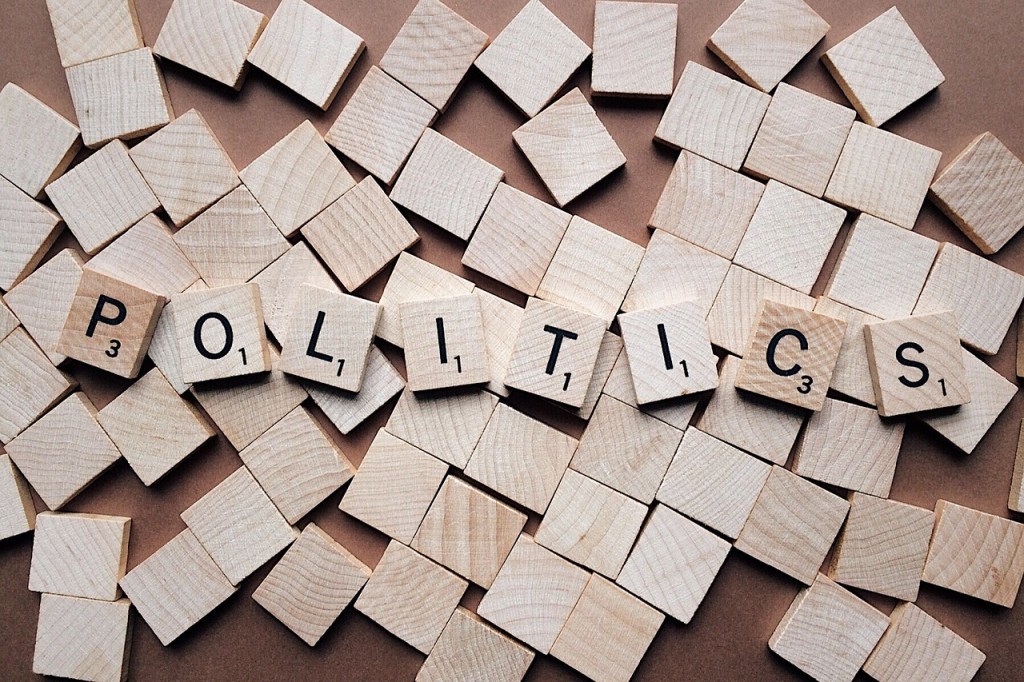Wooden letter tiles arranged to spell 'POLITICS', surrounded by unlettered tiles.