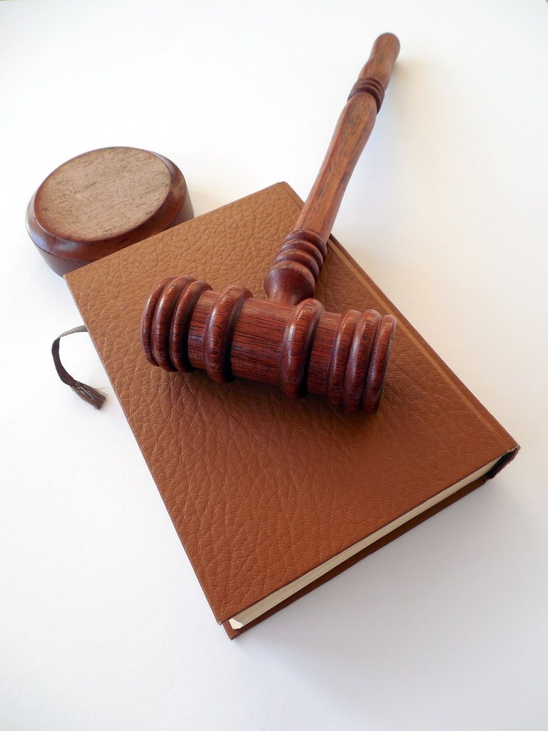 A wooden gavel resting on a brown leather-bound book with a circular wooden base in the background.