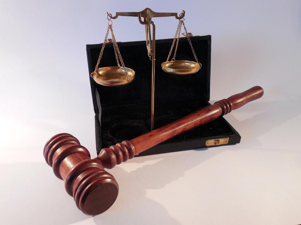 A wooden gavel next to a set of balance scales, symbolizing judgment and justice, placed on a white background.