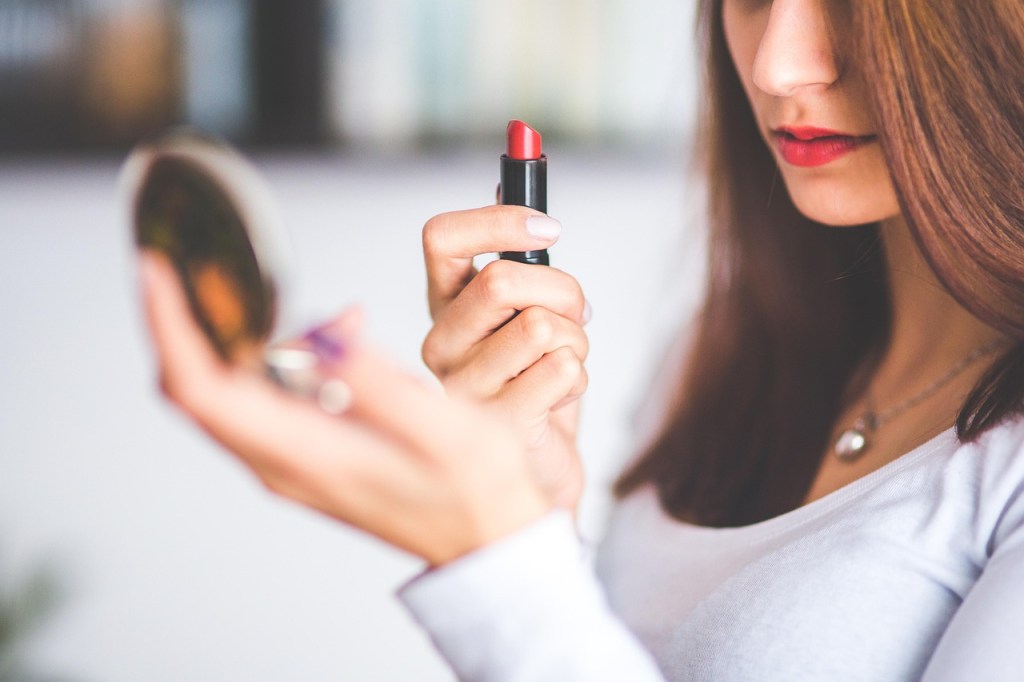 A woman holding a lipstick tube in one hand and a small mirror in the other, preparing to apply makeup.