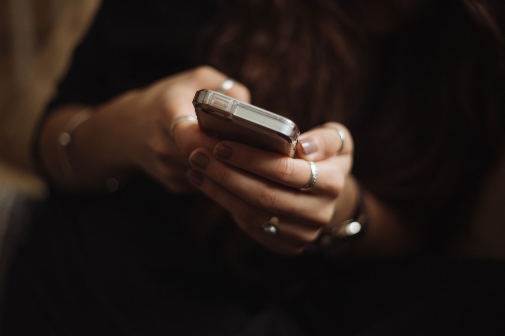 A close-up image of a person holding a smartphone, focusing on their hands adorned with rings and nail polish.