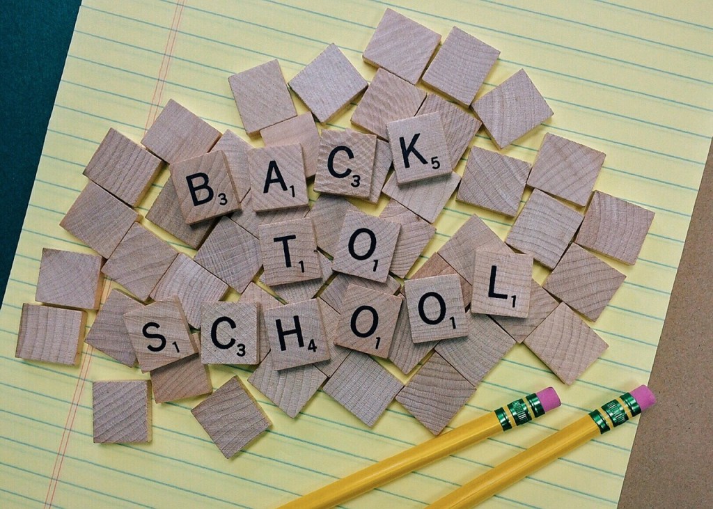Wooden letter tiles spelling 'BACK TO SCHOOL' on a yellow notepad, with two yellow pencils at the bottom.