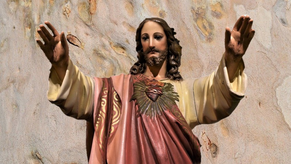 A statue of Jesus Christ with arms raised, depicting a gesture of blessing or welcome, set against a textured background.