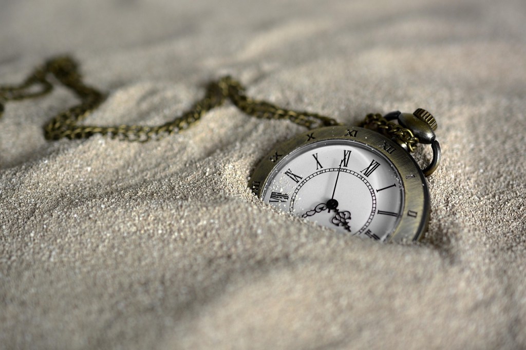 A vintage pocket watch partially buried in fine sand.