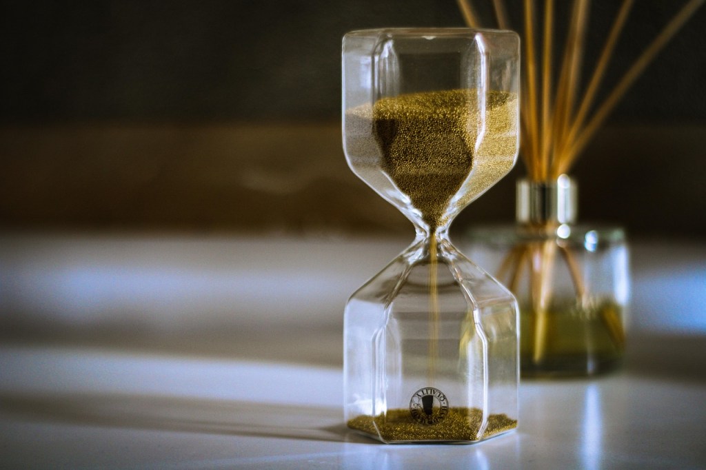 An hourglass with golden sand on a table, symbolizing the passage of time.