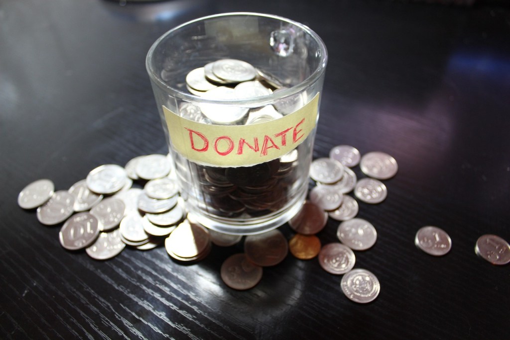 A glass container labeled 'DONATE' filled with coins, surrounded by scattered coins on a black surface.