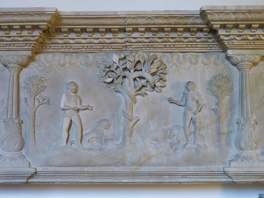 A stone relief depicting two figures standing near a tree, with one figure holding an object and the other gesturing. A small animal is present at the base of the tree, and a unicorn is shown near the second figure.