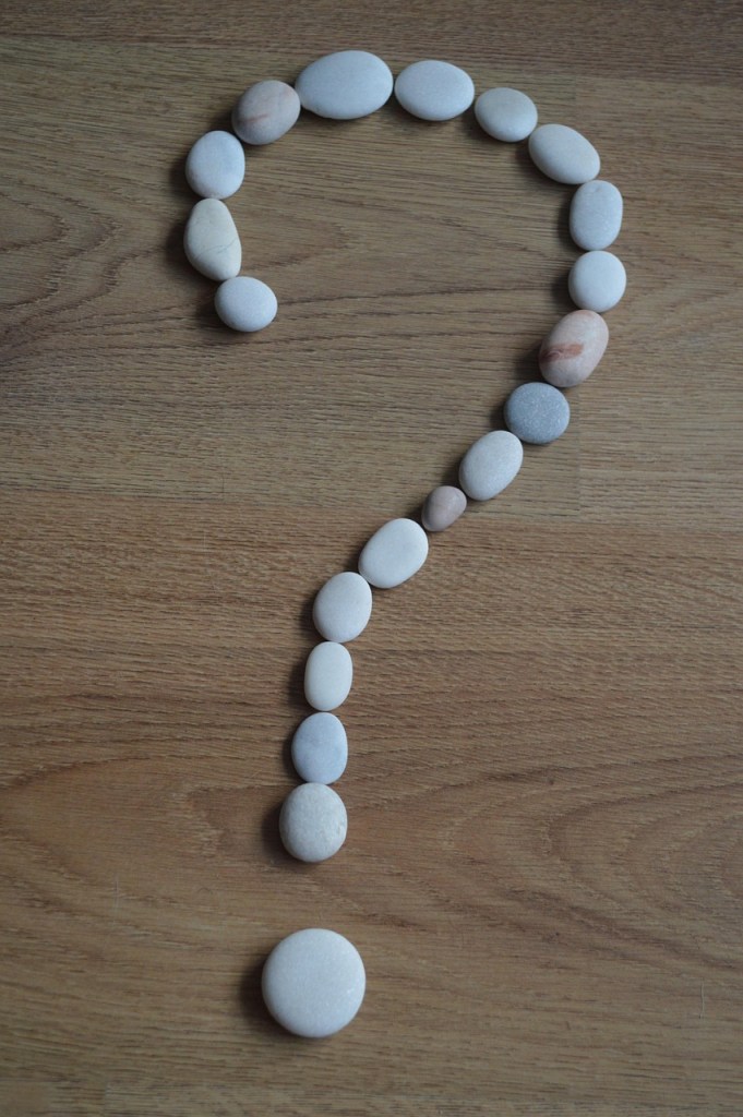 A collection of smooth, white pebbles arranged in the shape of a question mark on a wooden surface.