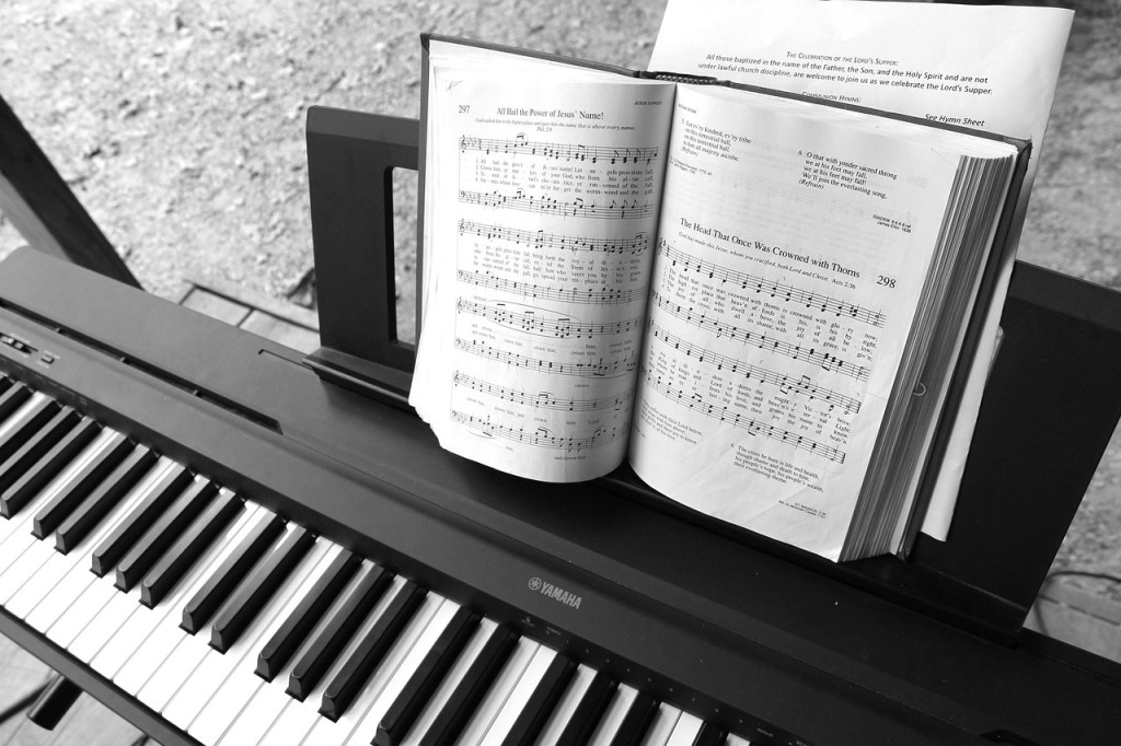 Close-up of a digital piano with sheet music open on the stand, displaying hymns and musical notation.